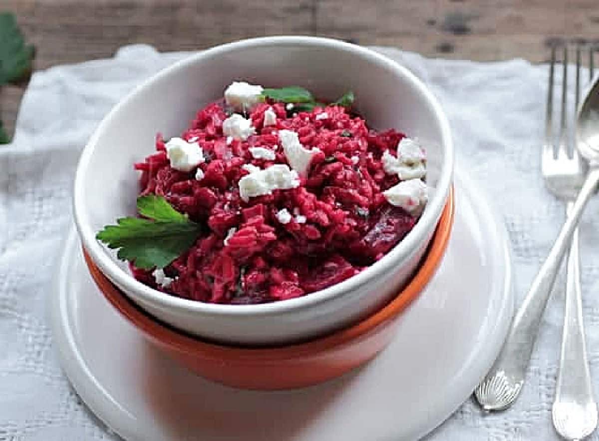 White bowl with beet risotto on a white napkin. Silver utensils. 
