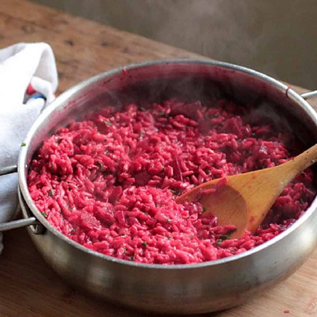 Metal skillet with beet risotto on a wooden table. 