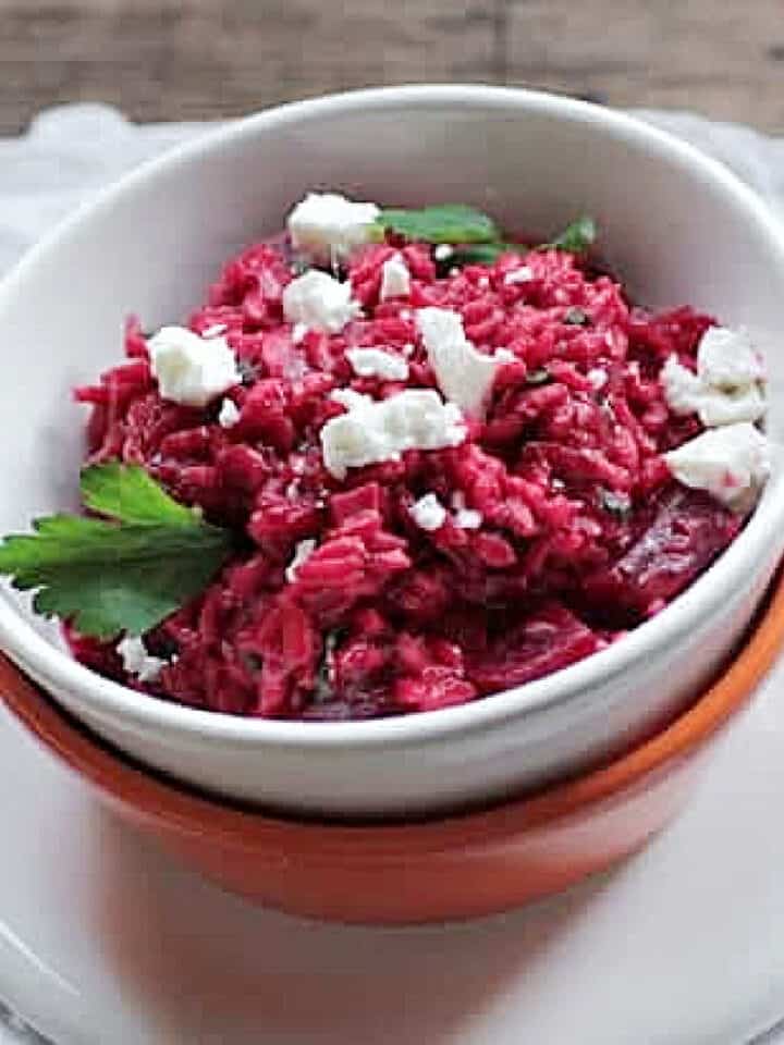 White bowl with beet risotto on a white napkin. Silver utensils.