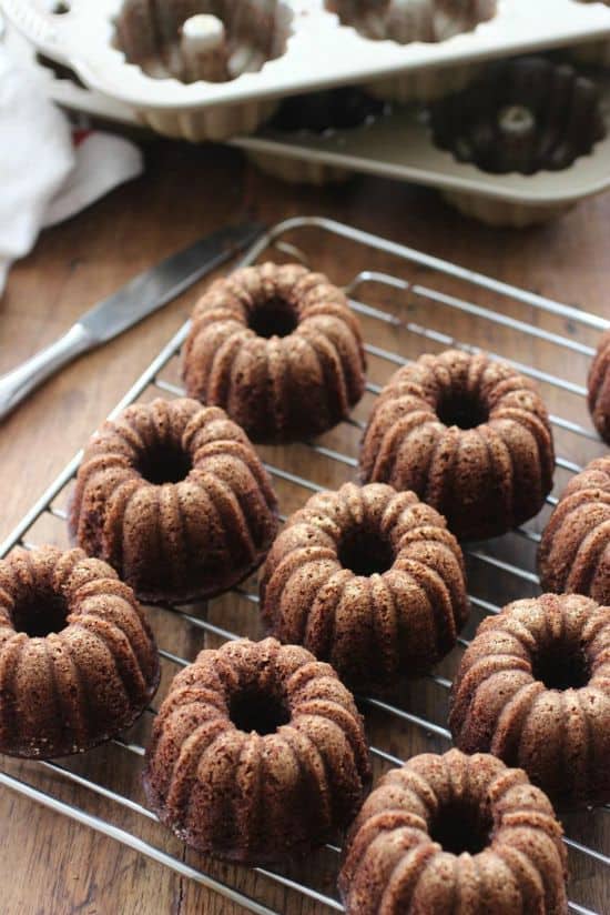 Several mini bundt cakes on wire rack, pans in the back, wooden table