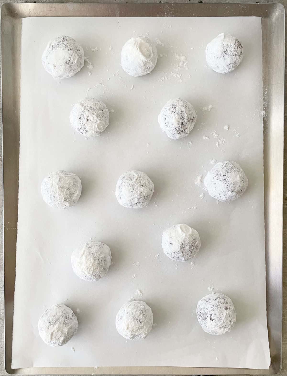 Powdered sugar coated cookie dough balls on parchment paper on a cookie sheet.
