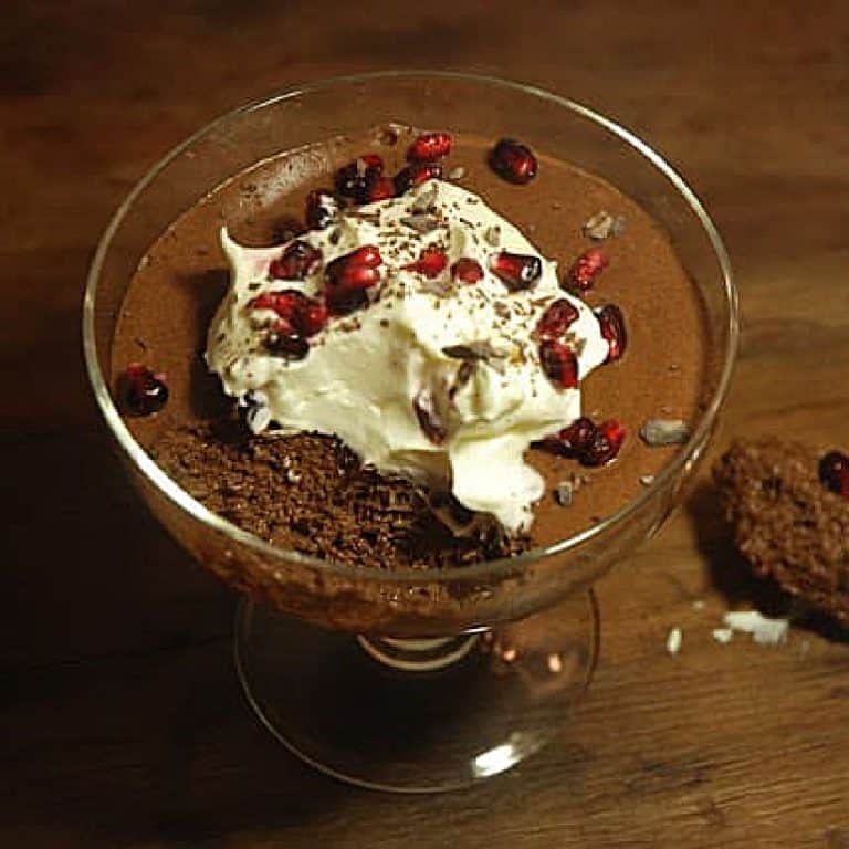 Glass cup with dark chocolate mousse with dollop of cream and pomegranate seeds. Wooden surface.