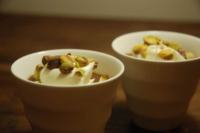 White ceramic cups with pistachios and whipped cream on a dark wooden surface.