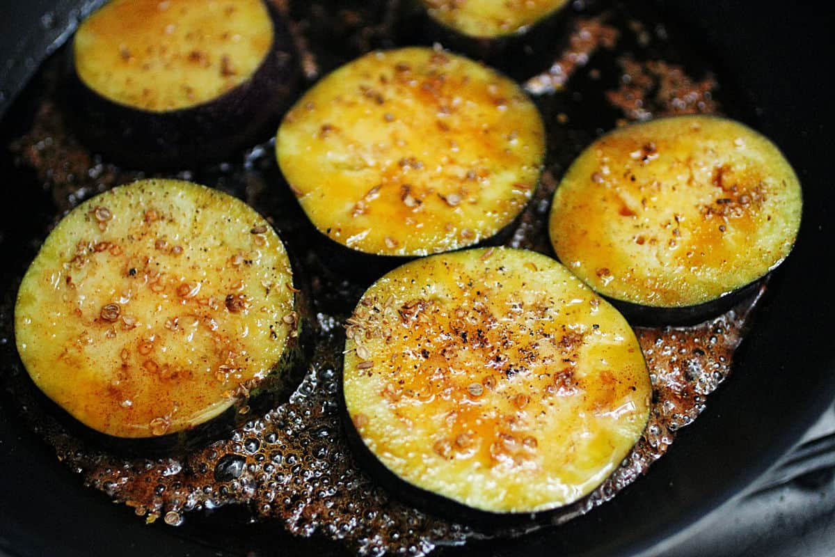 Cooking slices of eggplant with honey on a black skillet