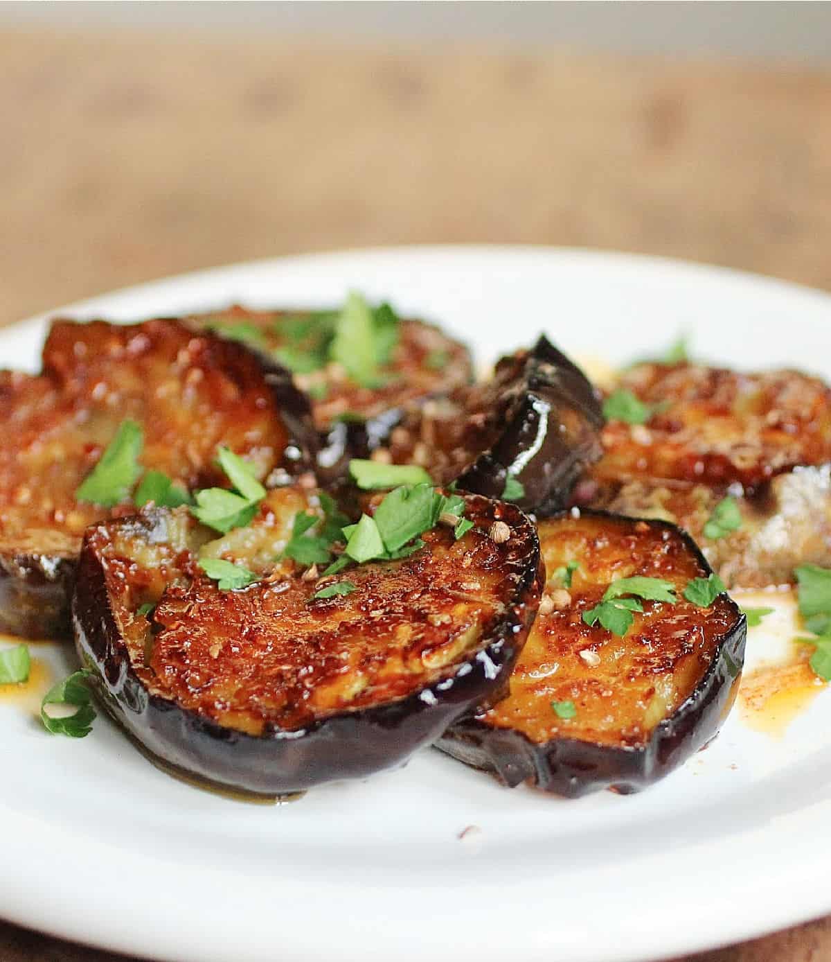 Partial view of white plate with eggplant rounds and herbs, wooden surface