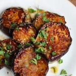 Close up of rounds of caramelized eggplant with parsley on white plate