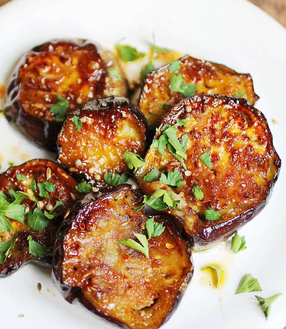Close up of rounds of caramelized eggplant with parsley on a white plate.