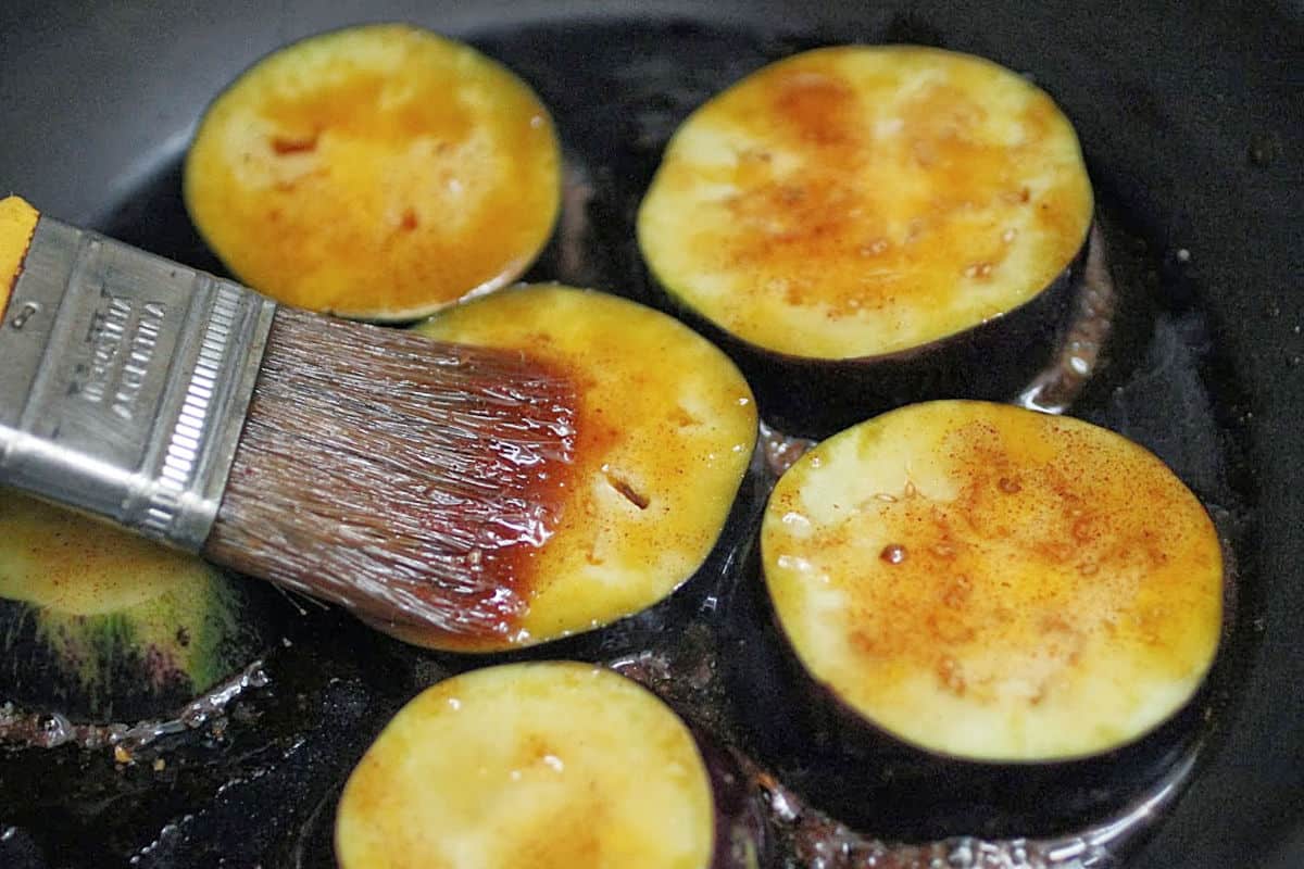 Brushing honey mixture over eggplant rounds in a black skillet.