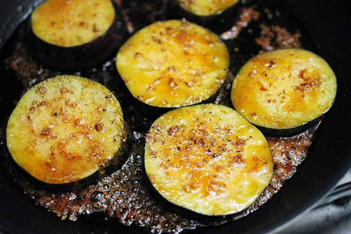 Cooking slices of eggplant with honey on a black skillet.