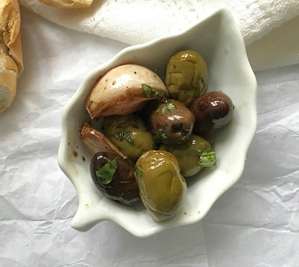 White leaf bowl with olives and garlic, white surface