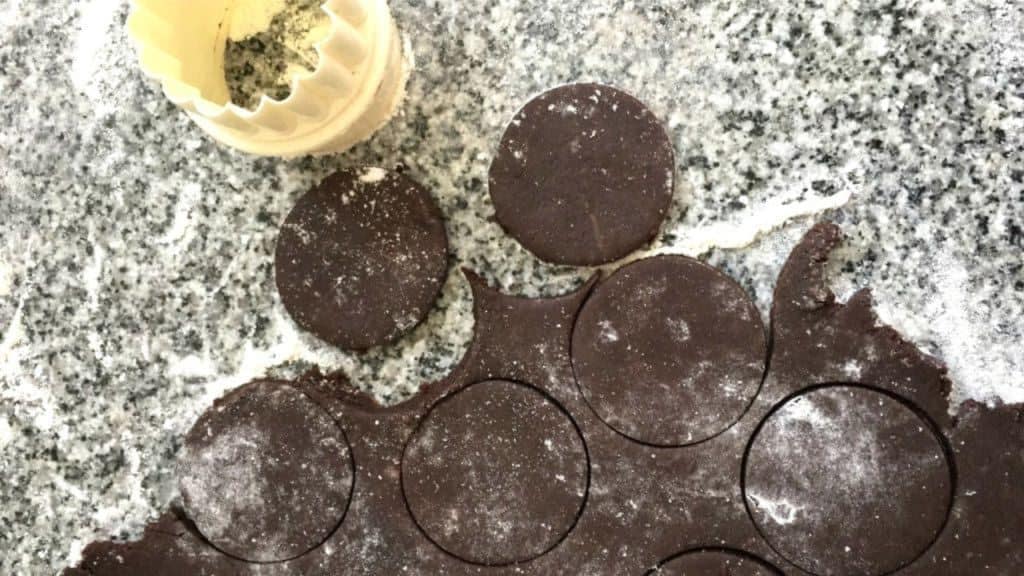 Chocotorta wafers being cut on grey marble counter. Plastic round cookie cutter.