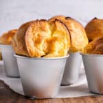 Tin molds with golden popovers. White paper on a wooden surface. Light gray background.