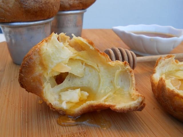 Opened popover on wooden board with rest of popovers and honey in background.