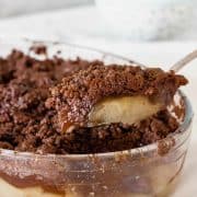 Serving chocolate apple crisp with silver spoon from glass dish