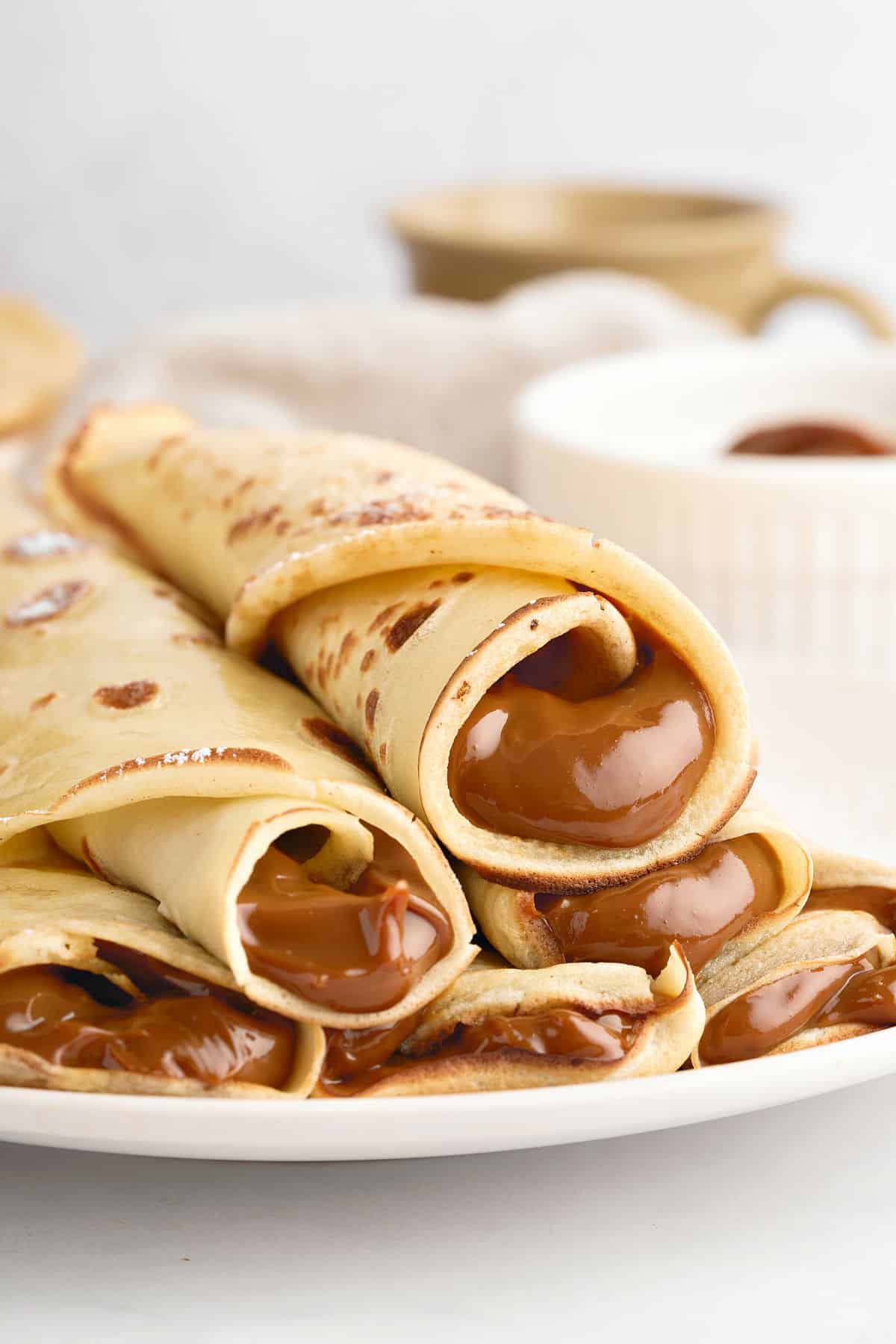 Pile of rolled dulce de leche thin pancakes on a white plate. White background. 