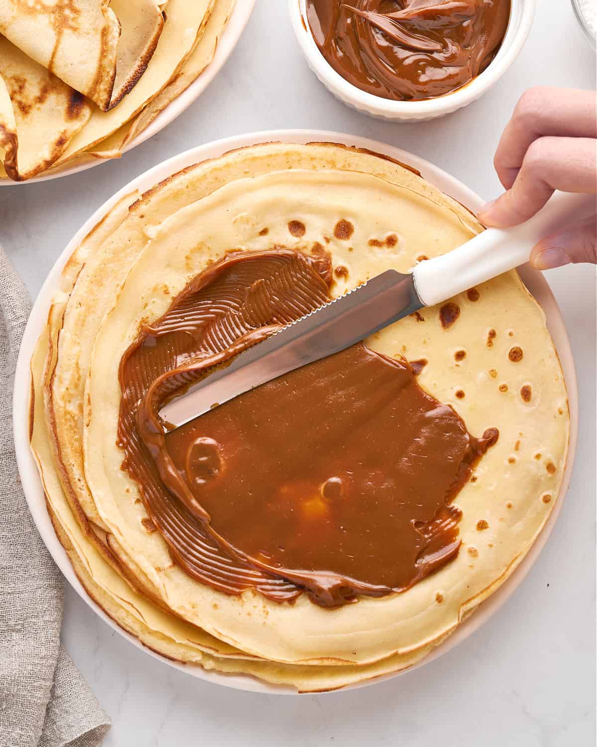 Spreading dulce de leche on thin recpes. White background. Top view.