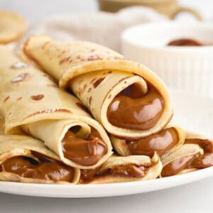 Rolled dulce de leche crepes on a white plate. White background.