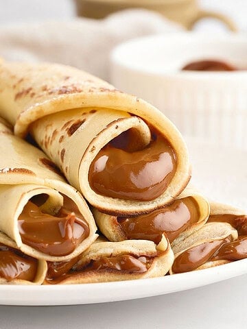 Rolled dulce de leche crepes on a white plate. White background.