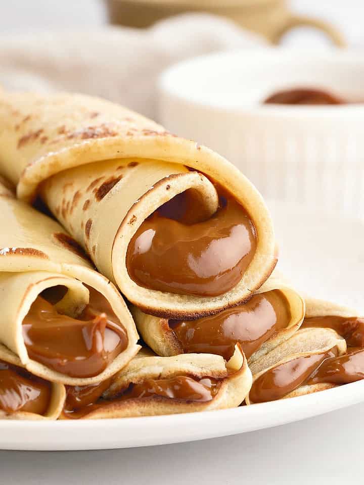 Rolled dulce de leche crepes on a white plate. White background.