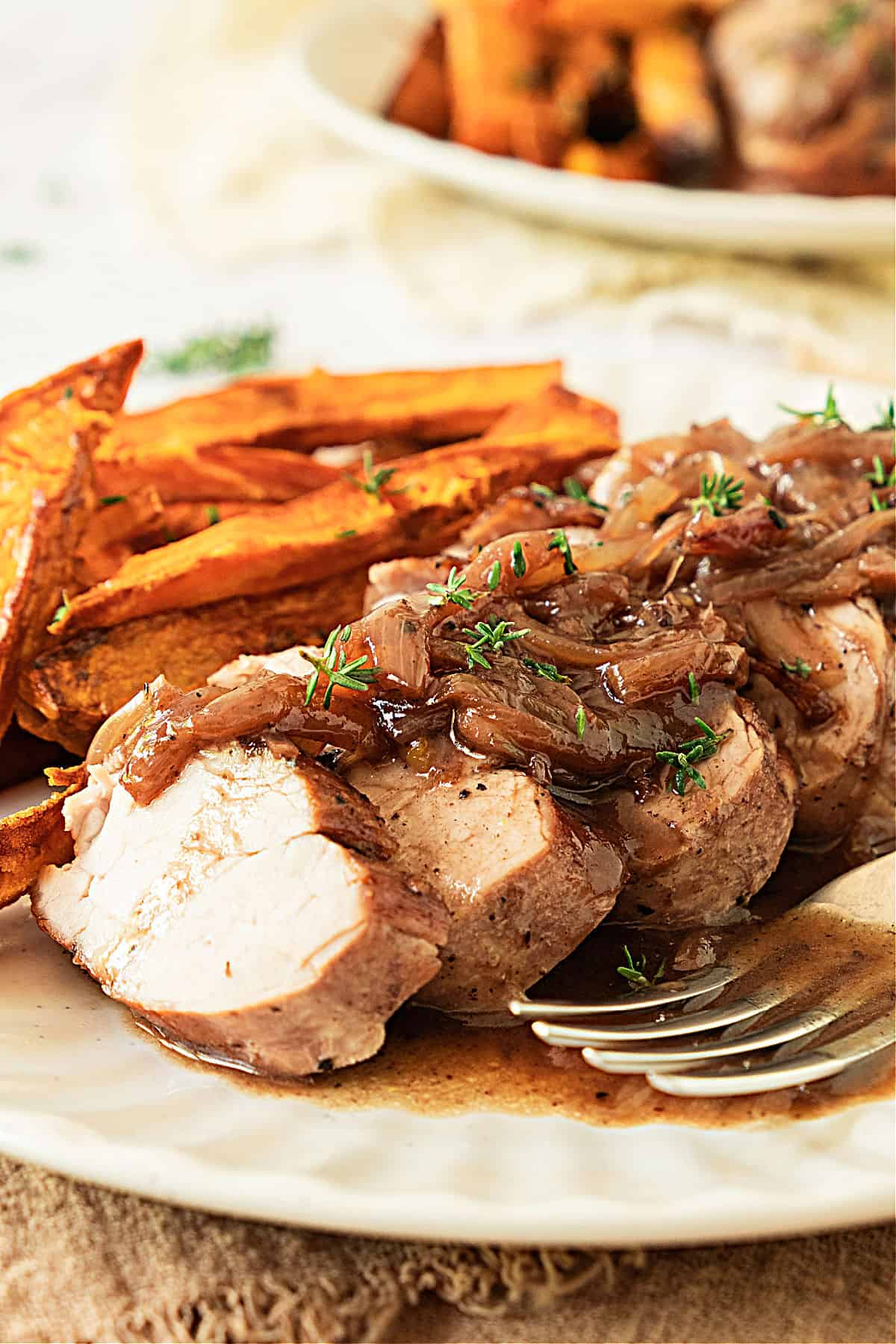 Slices of pork tenderloin with port shallot sauce and sweet potatoes. White plate, silver fork.