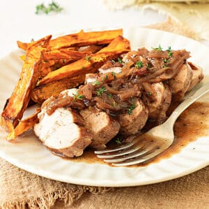 White plate with serving of pork loin, shallot sauce and roasted sweet potatoes. Beige background.