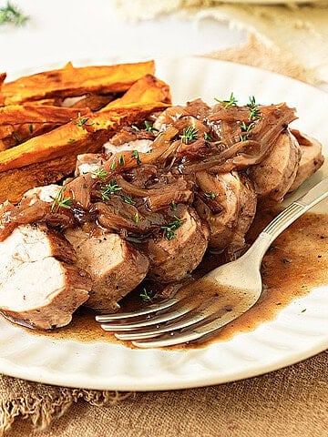 White plate with serving of pork loin, shallot sauce and roasted sweet potatoes. Beige background.