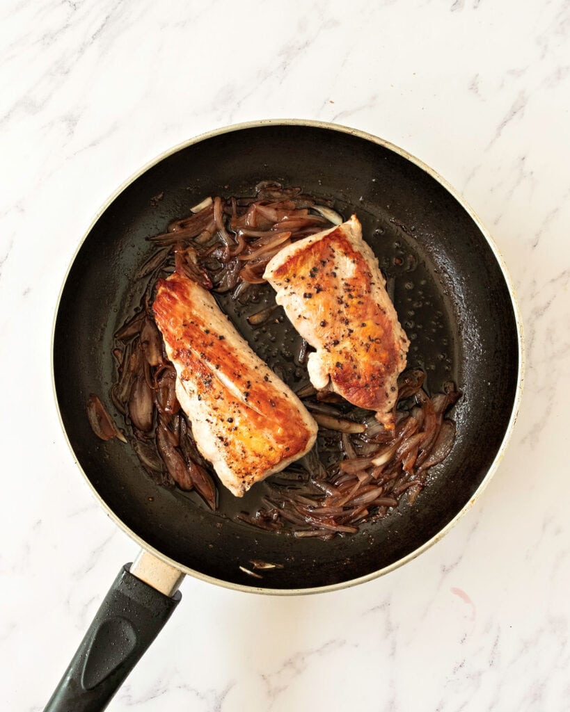 Two pork loins with shallot sauce in a black skillet. Top view. White background.