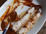White ceramic oval dish with two dulce de leche crepes, spoon, smeared milk jam