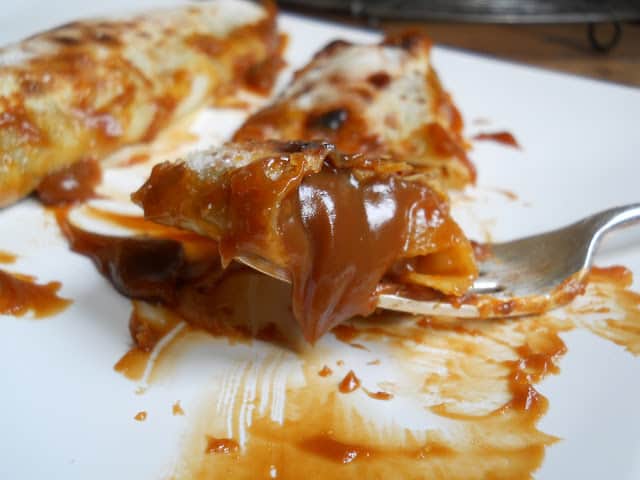 Fork with bite of dulce de Leche crepe on white plate. 
