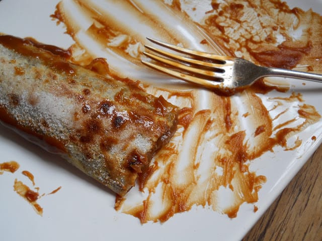 Half eaten dulce de leche crepe on white plate with silver fork. 