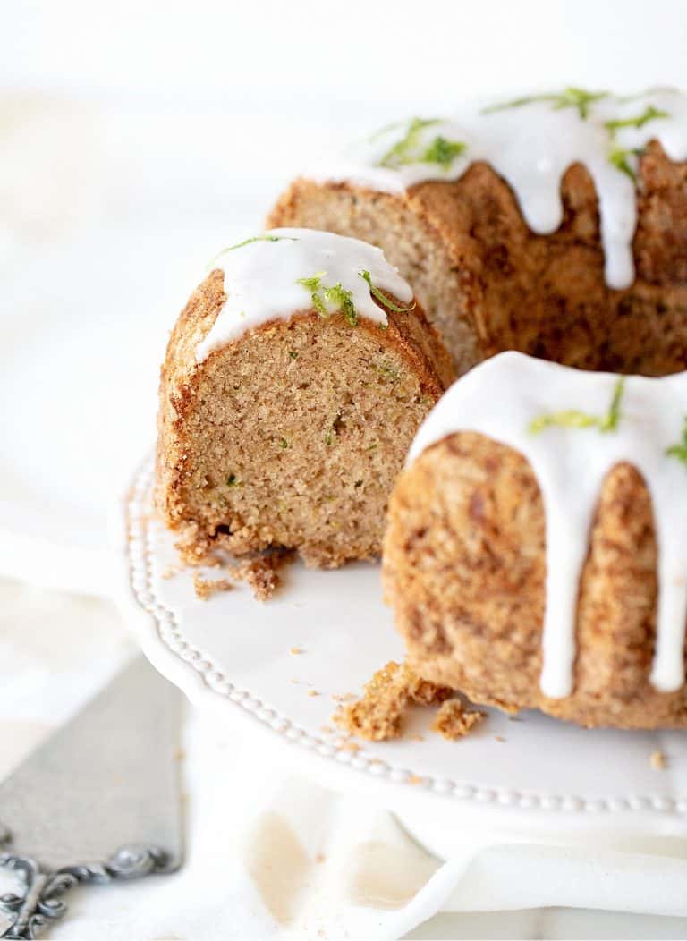 Partial view of glazed bundt cake on white cake stand, silver cake server, white background