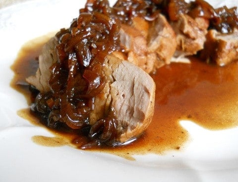 Close up of sliced pork tenderloin with port shallot sauce on a white plate.