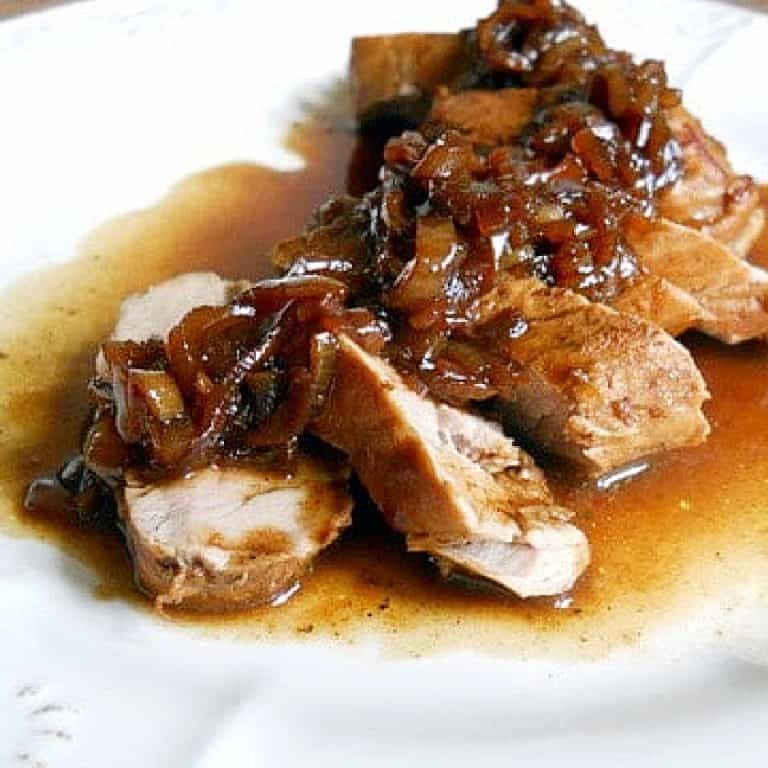 Sliced pork loin with port shallot sauce on a white plate.