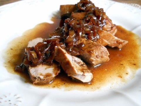 White plate with pork loin in slices with dark shallot sauce. 