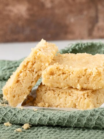 Close up of shortbread squares leaning and stacked on a green cloth with a brown background.