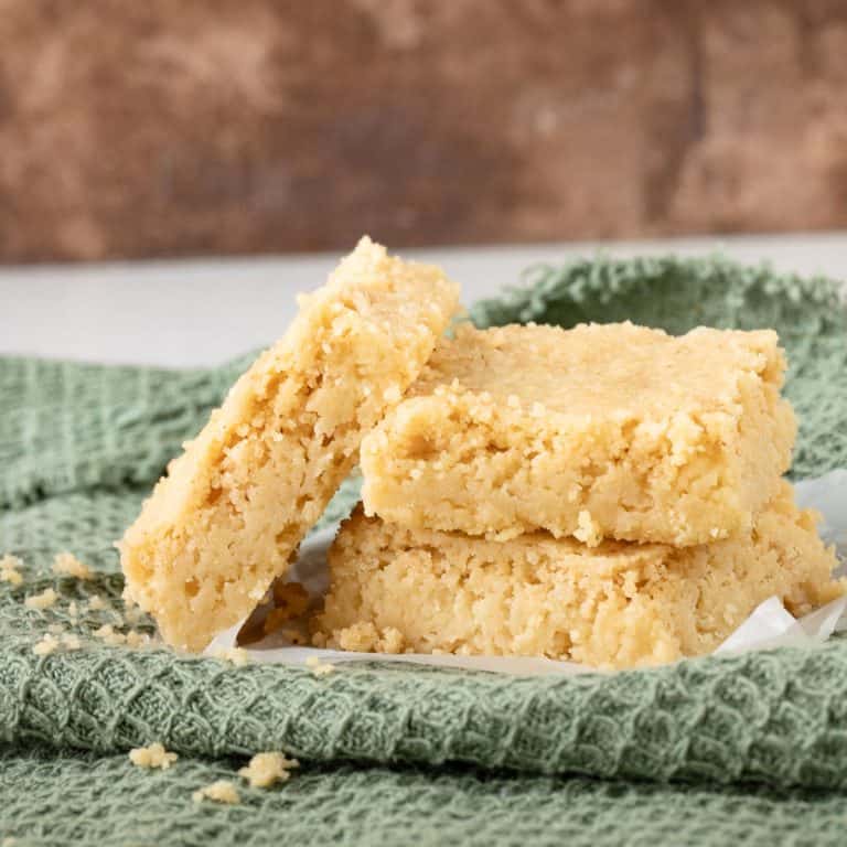 Close up of shortbread squares leaning and stacked on a green cloth with a brown background.