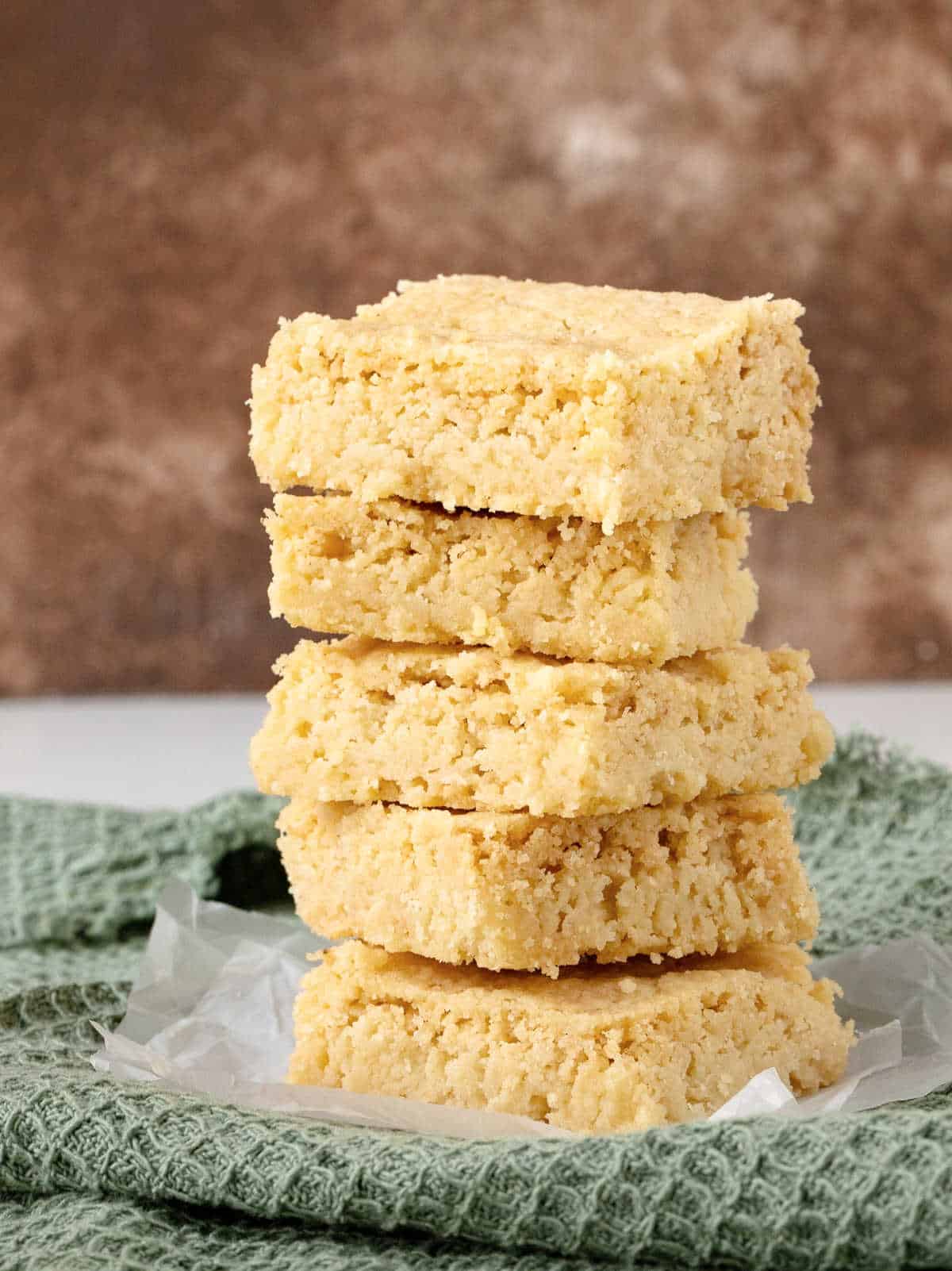 Stack of brown butter shortbread squares on a green cloth with a brown background. 