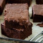 Stacked squares of glazed chocolate cake on metal square pan