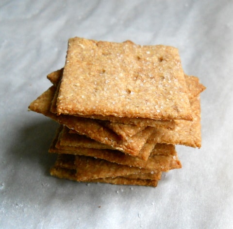 Stack of homemade Wheat Thin Crackers on white parchment paper. 
