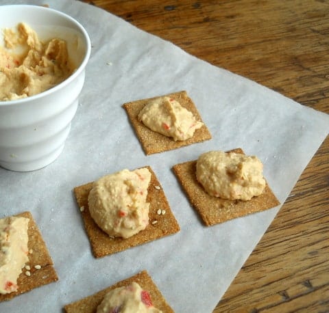 Homemade Wheat Thin Crackers with hummus on white parchment paper on a wooden table. 