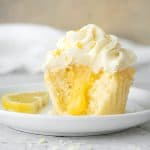 Frosted lemon curd cupcake half on a white plate. White and beige background, grey surface.