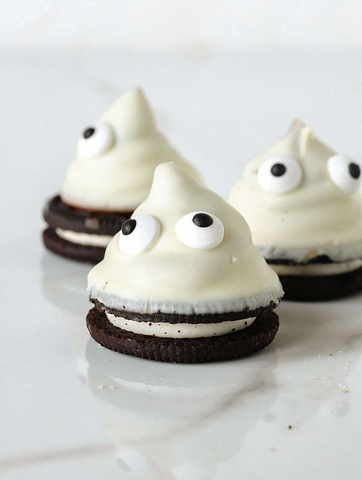 Three cones made of oreo cookies and dulce de leche covered in white chocolate with candy eyes. White marble surface. 