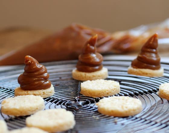Rounds of shortbread on a wire rack, some with mounds of dulce de leche filling. 