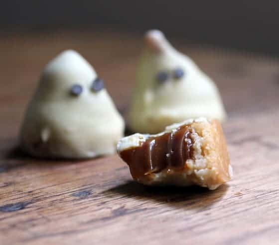 Wooden surface with two white chocolate ghosts and one with exposed dulce de leche center. 