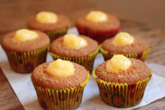 Lemon curd filled cupcakes in yellow paper cups on white paper on a wooden table. 
