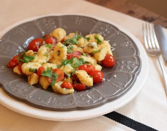 Grey plate of potato gnocchi with cherry tomatoes on white tablecloth.