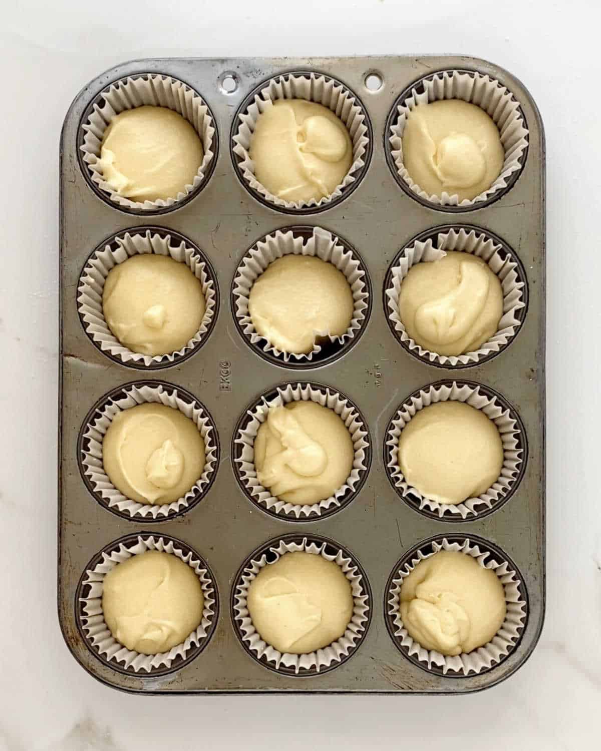 Top view of metal cupcake pan with lemon cake batter. White marble surface.