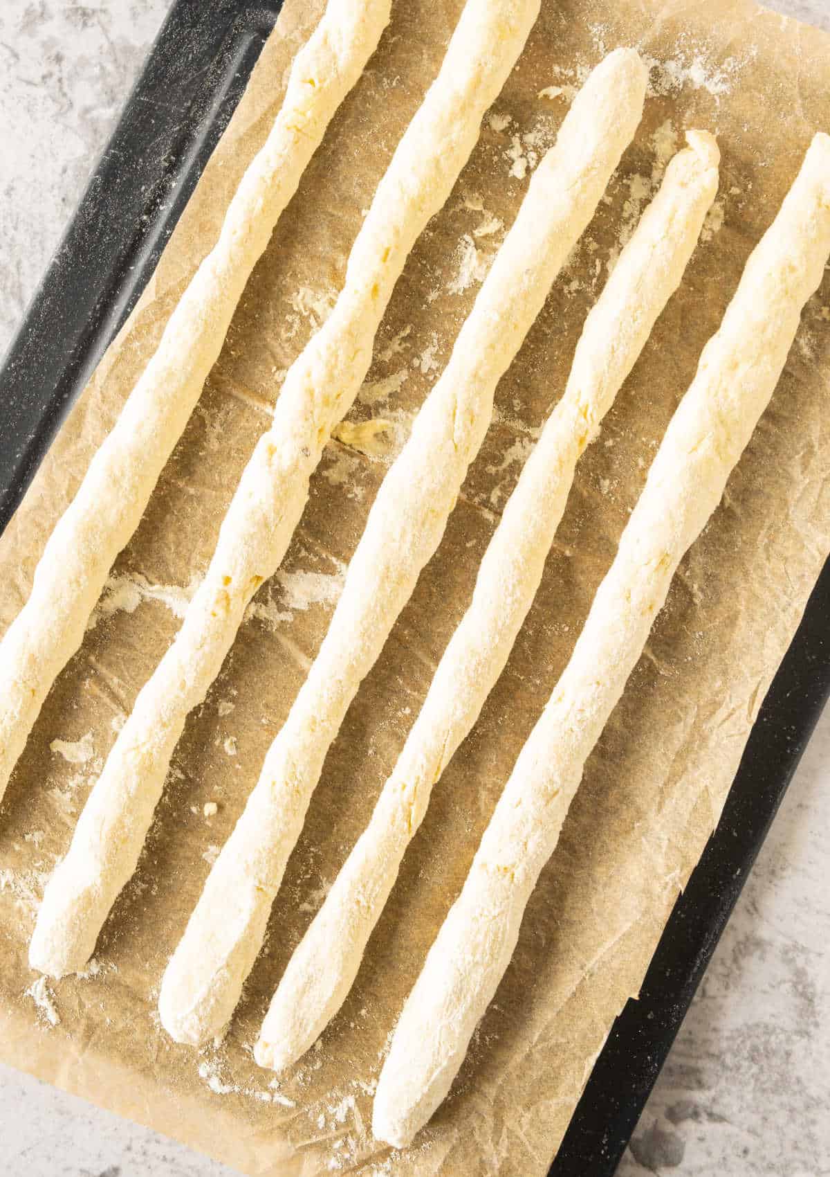Strips of potato gnocchi dough on beige paper set on a black oven tray.