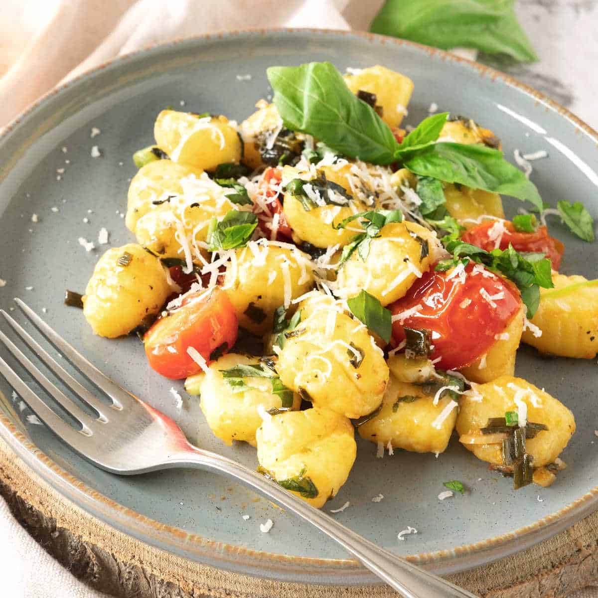 Grey plate with potato gnocchi serving with basil and tomatoes. A silver fork.