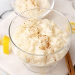 Close up of cinnamon rice pudding served in glass cups on a white marble surface.